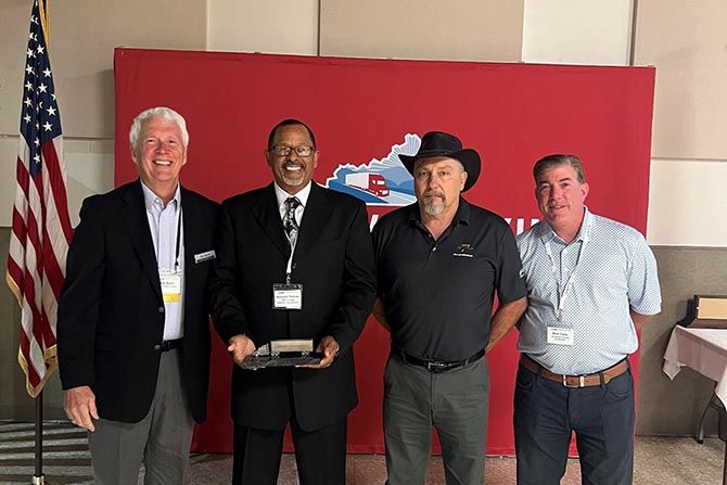 2025 KTA Annual Conference Recap; Four men stand smiling in front of a red backdrop with a logo. One man holds an award. An American flag is visible on the left. The mood is celebratory.