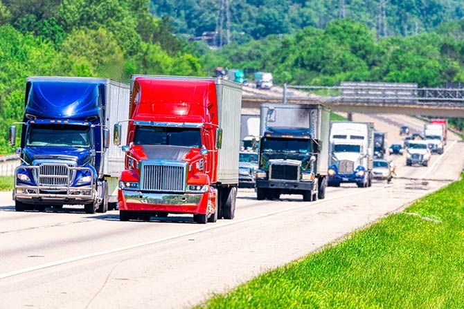 The Benefits of Membership; A bright red and a blue semi-truck drive side by side on a highway surrounded by lush greenery, conveying a sense of bustling transportation.