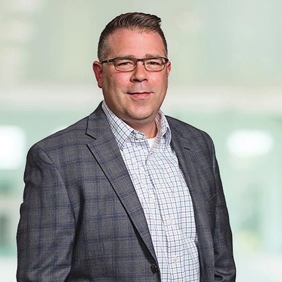 Member Spotlight: Getting To Know Troy Hogan With KSM; A confident man in glasses and a plaid suit jacket smiles warmly against a soft-focus background, conveying a professional and approachable tone.
